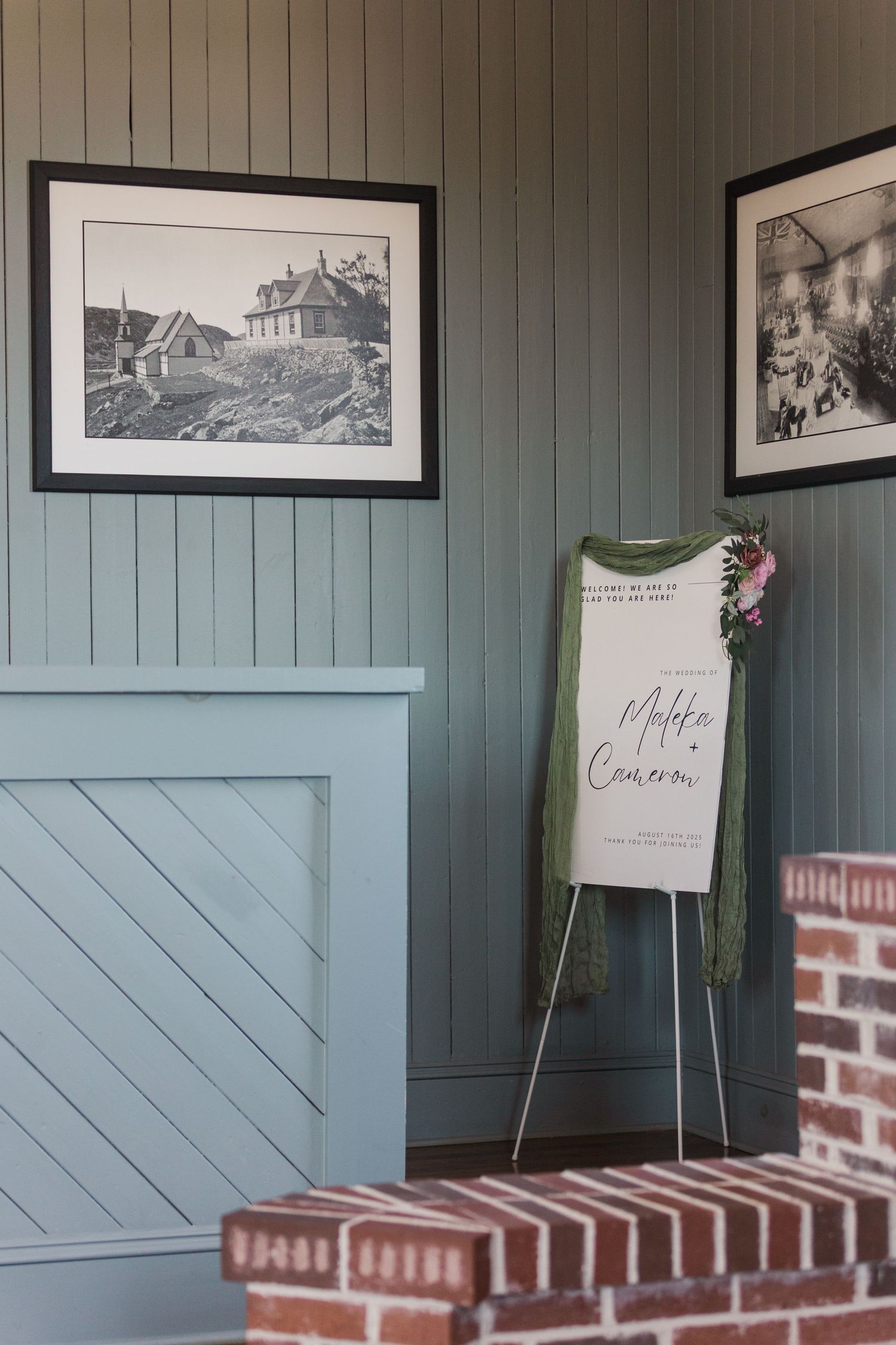 A framed black and white coastal artwork hangs on blue-gray paneled walls above red brick steps with an easel display.