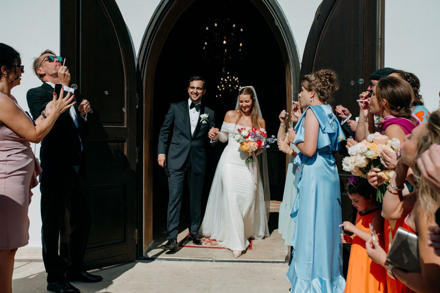 Newly married couple walking out of the church doors, smiling and holding hands