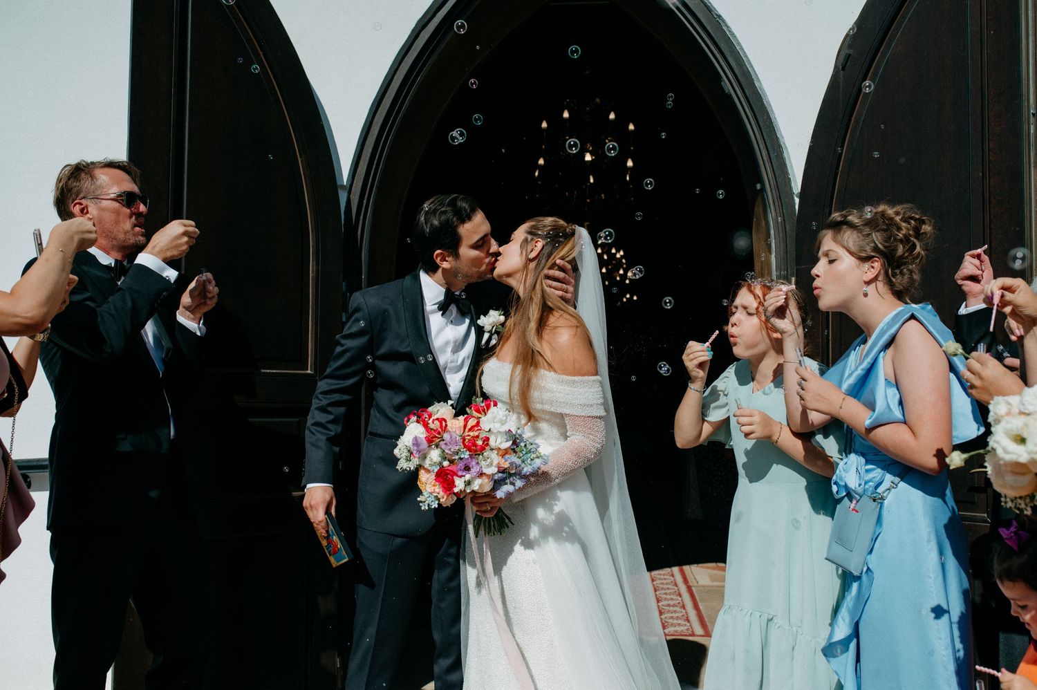 Newly married couple walking out of the church doors, smiling and holding hands