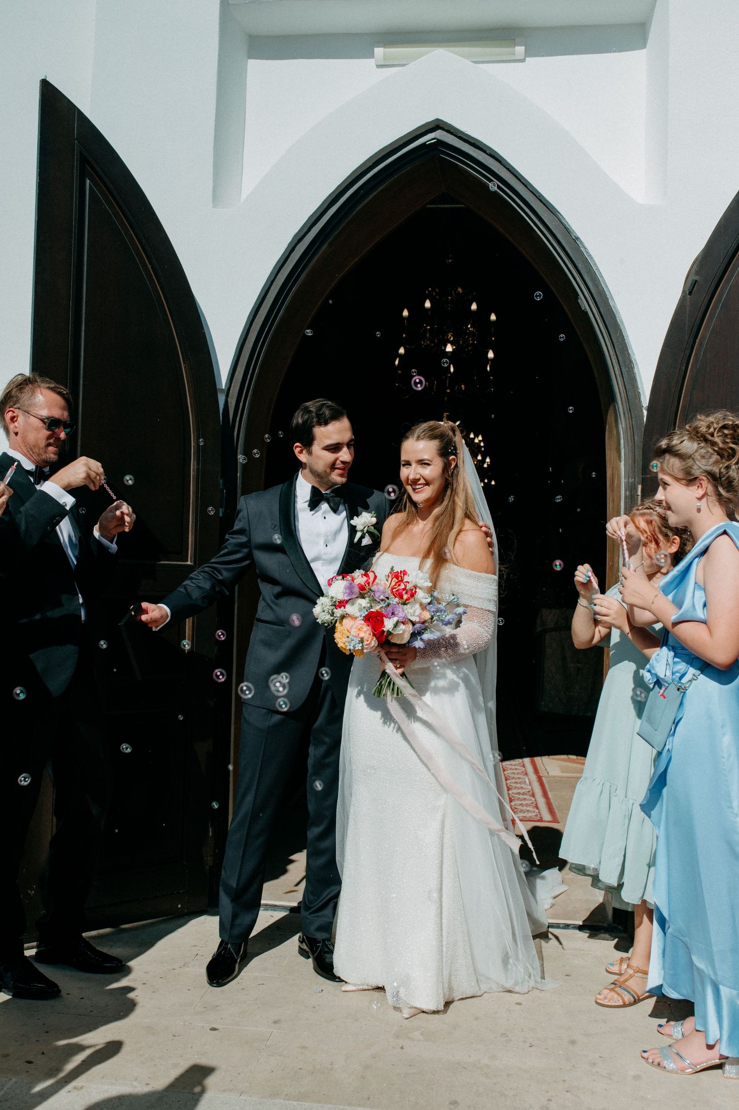 Newly married couple walking out of the church doors, smiling and holding hands