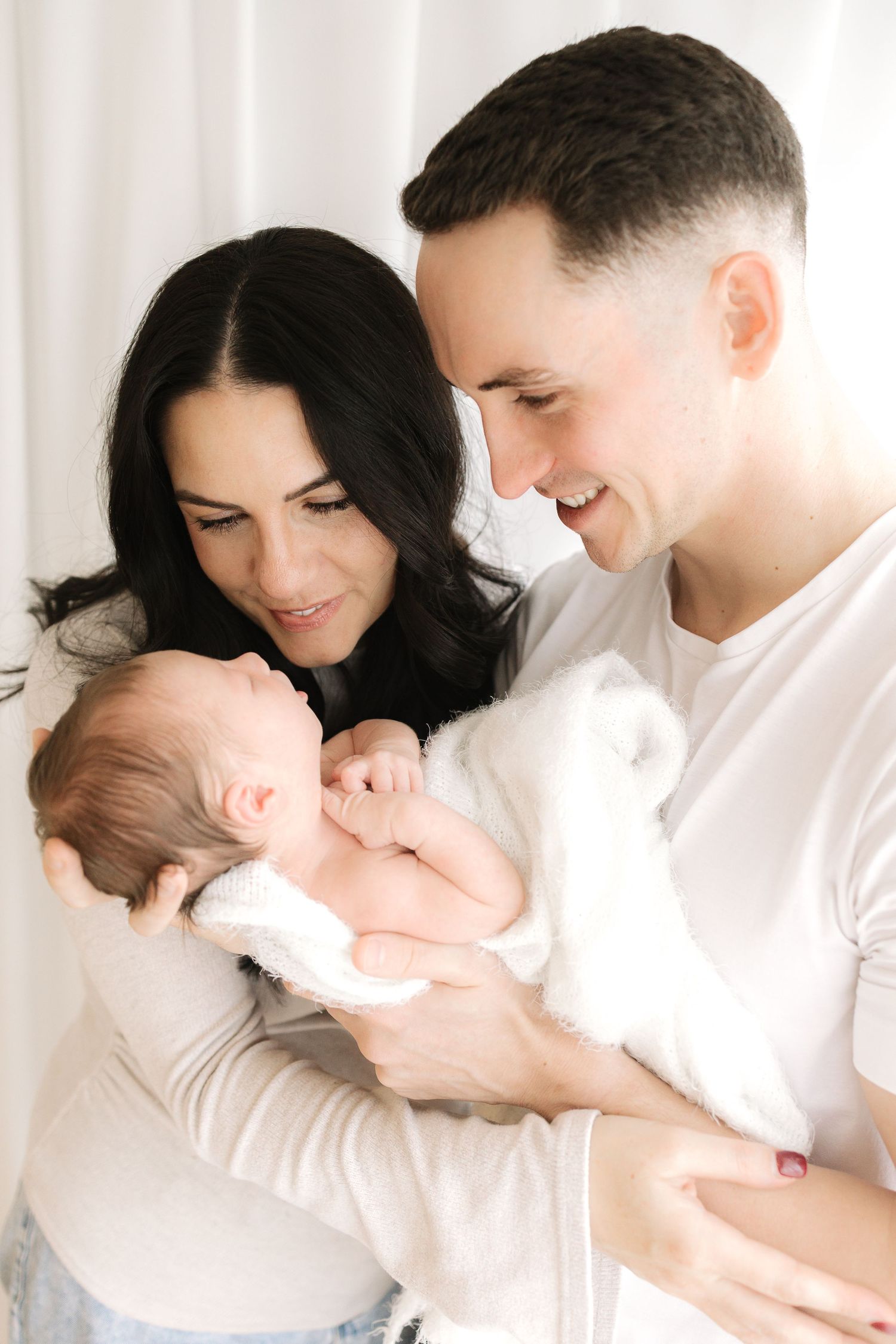 A baby lies on white bedding while laughing and kicking their legs in a playful sequence of movements.