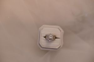 Engagement ring with brilliant diamond solitaire displayed from multiple angles against blush pink background.