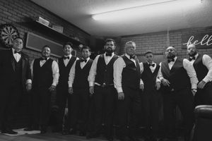 A black and white photograph shows a row of performers in formal attire lined up for a group portrait.