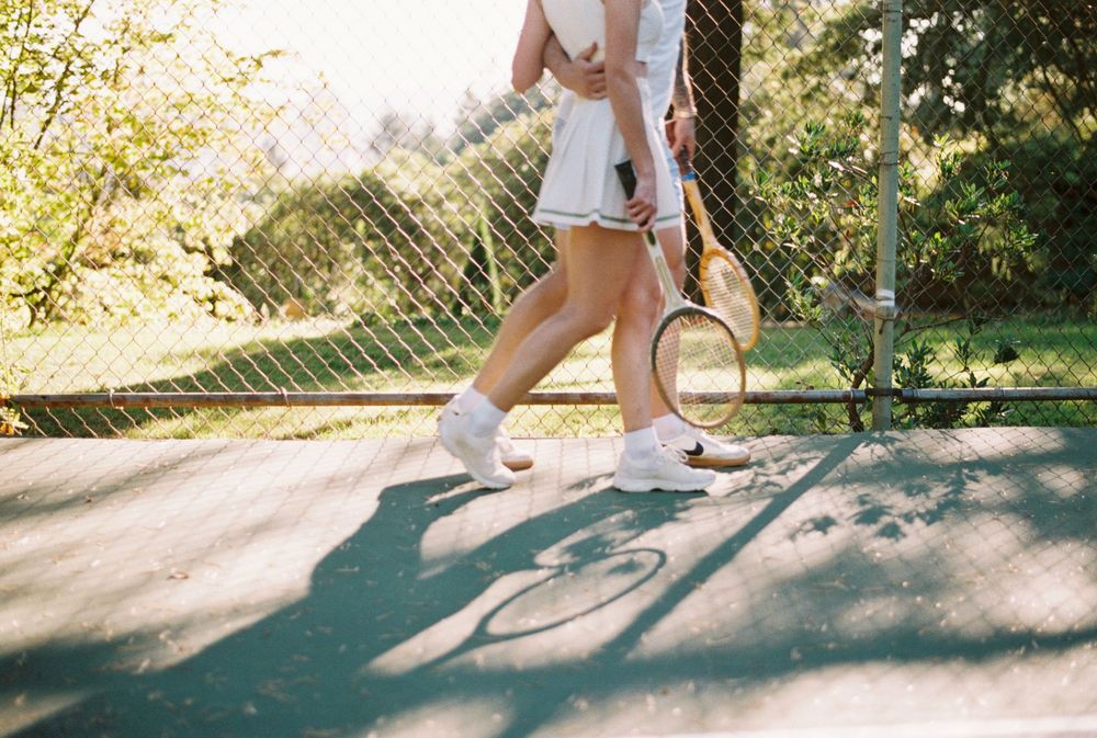 Low angle view of tennis players walking across a sunny court casting long shadows on the ground during sunset.