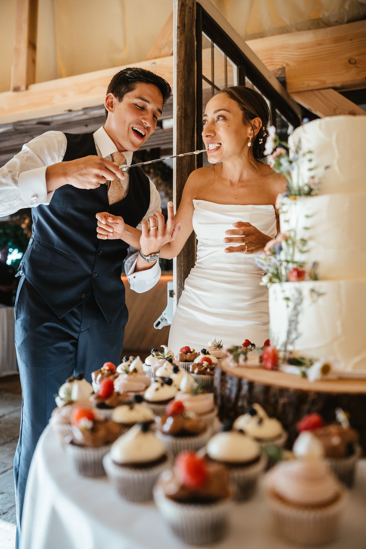 Wedding couple shares a joyful moment while feeding each other cupcakes at their reception celebration.