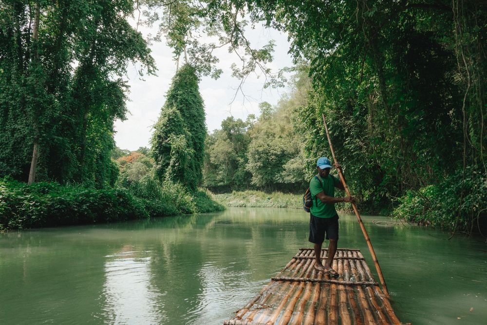 Bamboo raft floating down a serene river surrounded by lush green trees and vegetation.