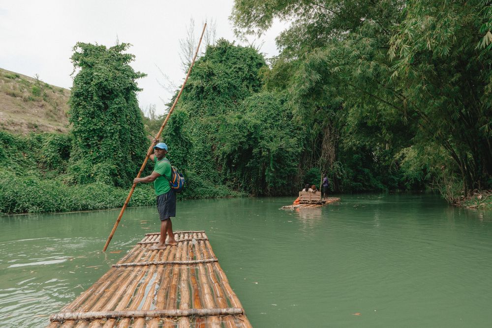 Group of adventurers navigate turquoise waters on handmade bamboo rafts through a scenic river gorge.
