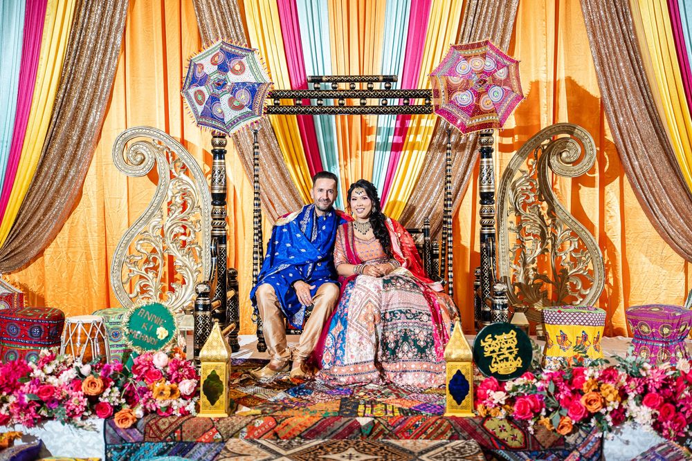 Elegant wedding stage decorated with colorful drapes, floral arrangements and ornate furniture in warm lighting.
