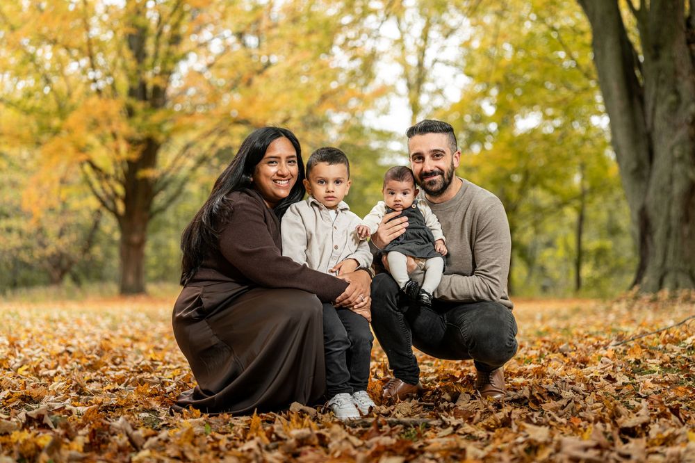 A couple sits together on fallen autumn leaves in a park during a romantic fall photoshoot.