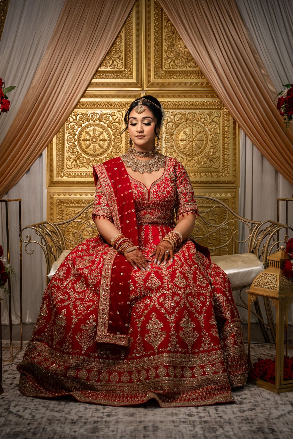 A traditional South Asian bridal lehenga in rich red and gold embroidery displayed in an ornate venue with golden decor.