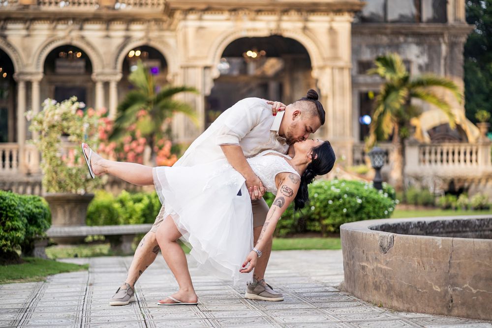 Dancing couple in formal attire pose elegantly on classic stone architecture backdrop.