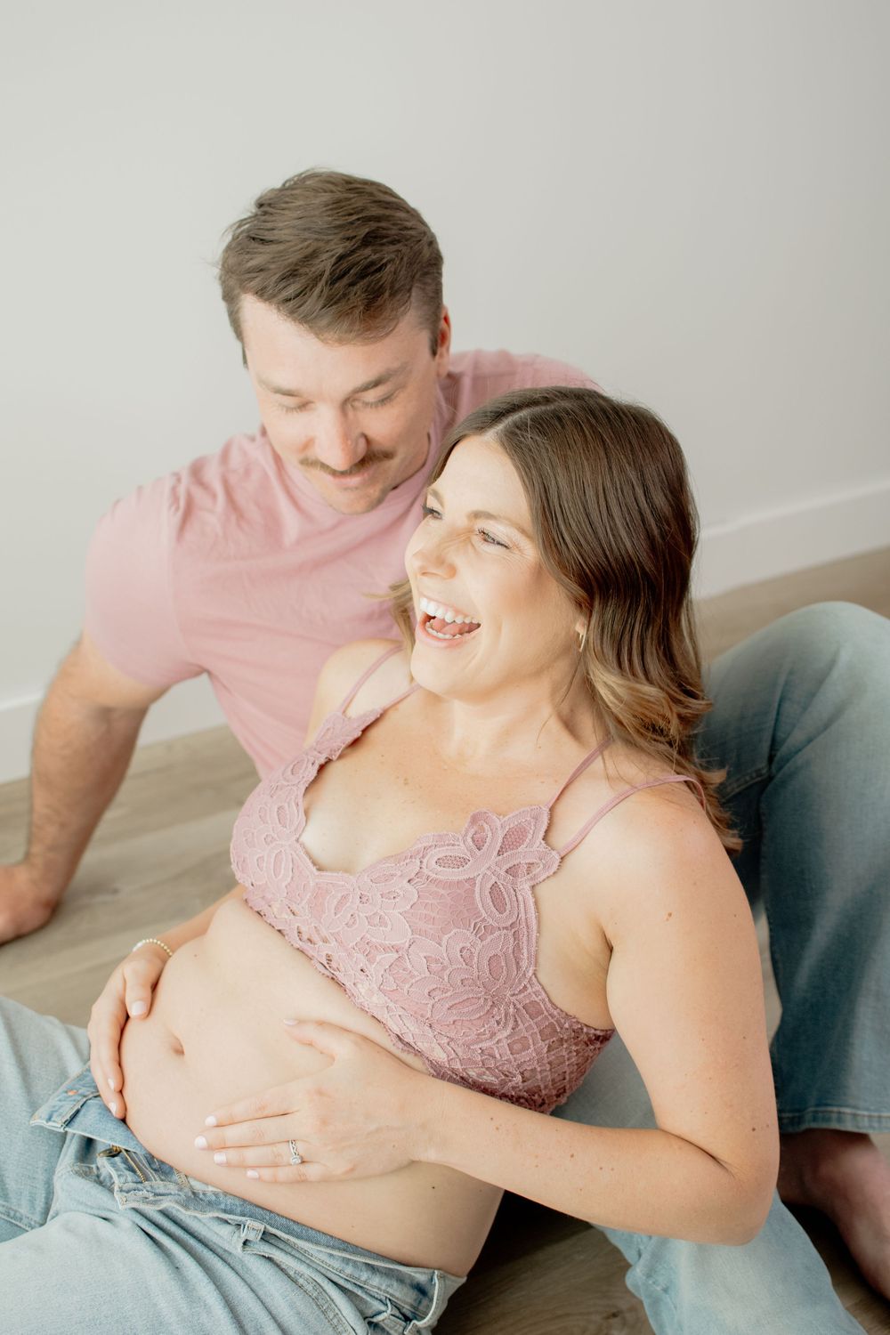 Expectant couple shares tender moment while relaxing on gray couch during maternity photoshoot.