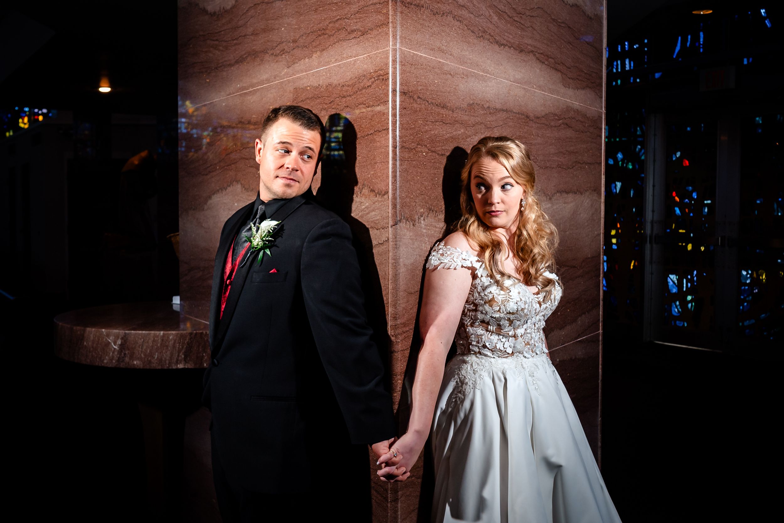 Couple poses against textured wall in formal wedding attire during artistic portrait session.