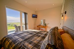 Modern apartment interior with sunny balcony view and comfortable queen bed in neutral tones.