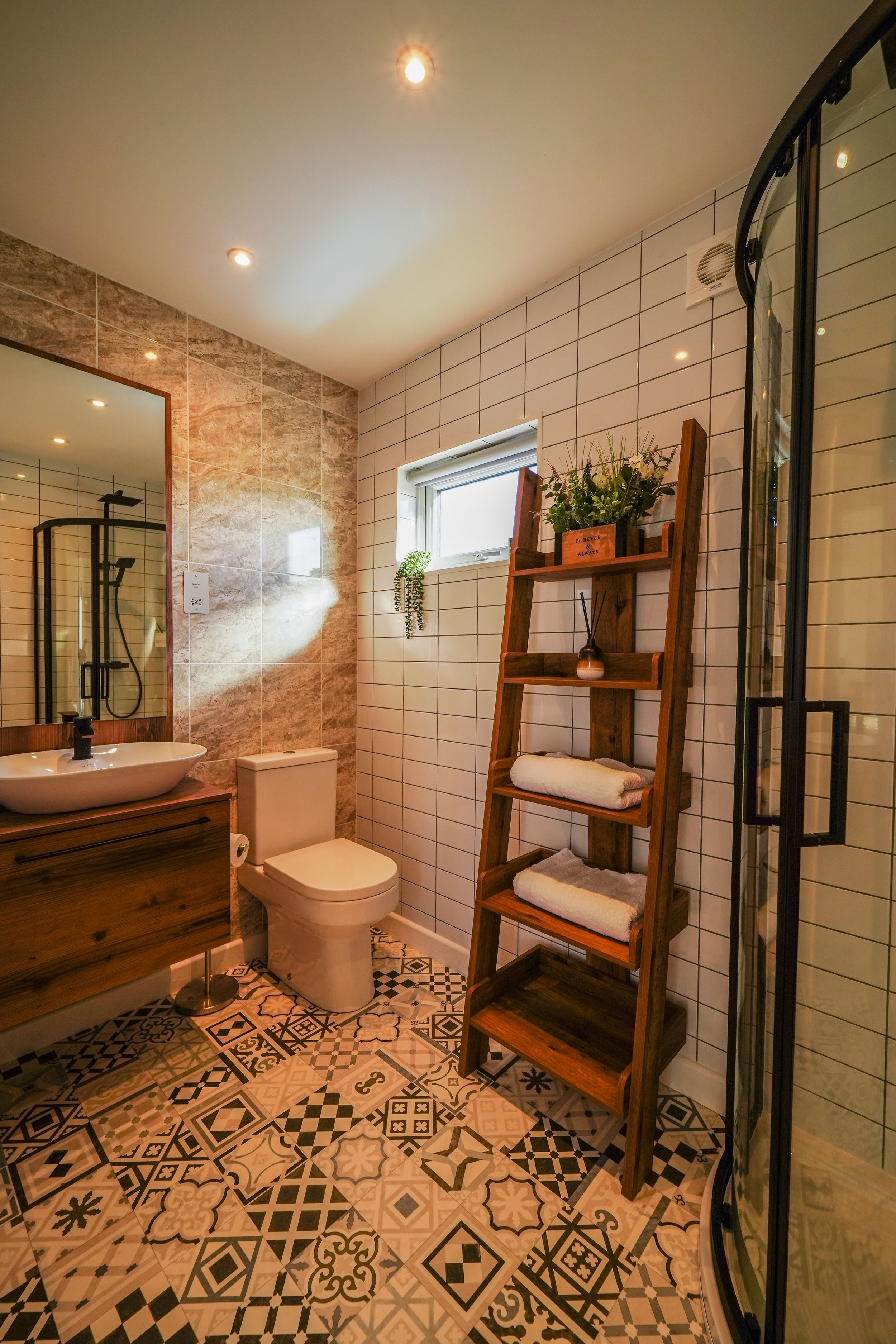 Modern bathroom with patterned floor tiles, wooden vanity, and ladder shelf storage against white tiled walls.