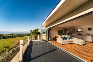 Modern luxury home deck with wooden flooring and white seating area opens to panoramic countryside views against blue sky.