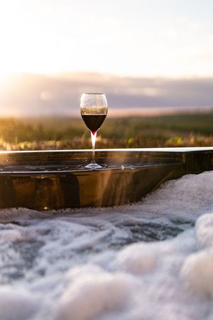 A glass of wine sits on a snowy ledge at sunset with a scenic mountain landscape in the background.