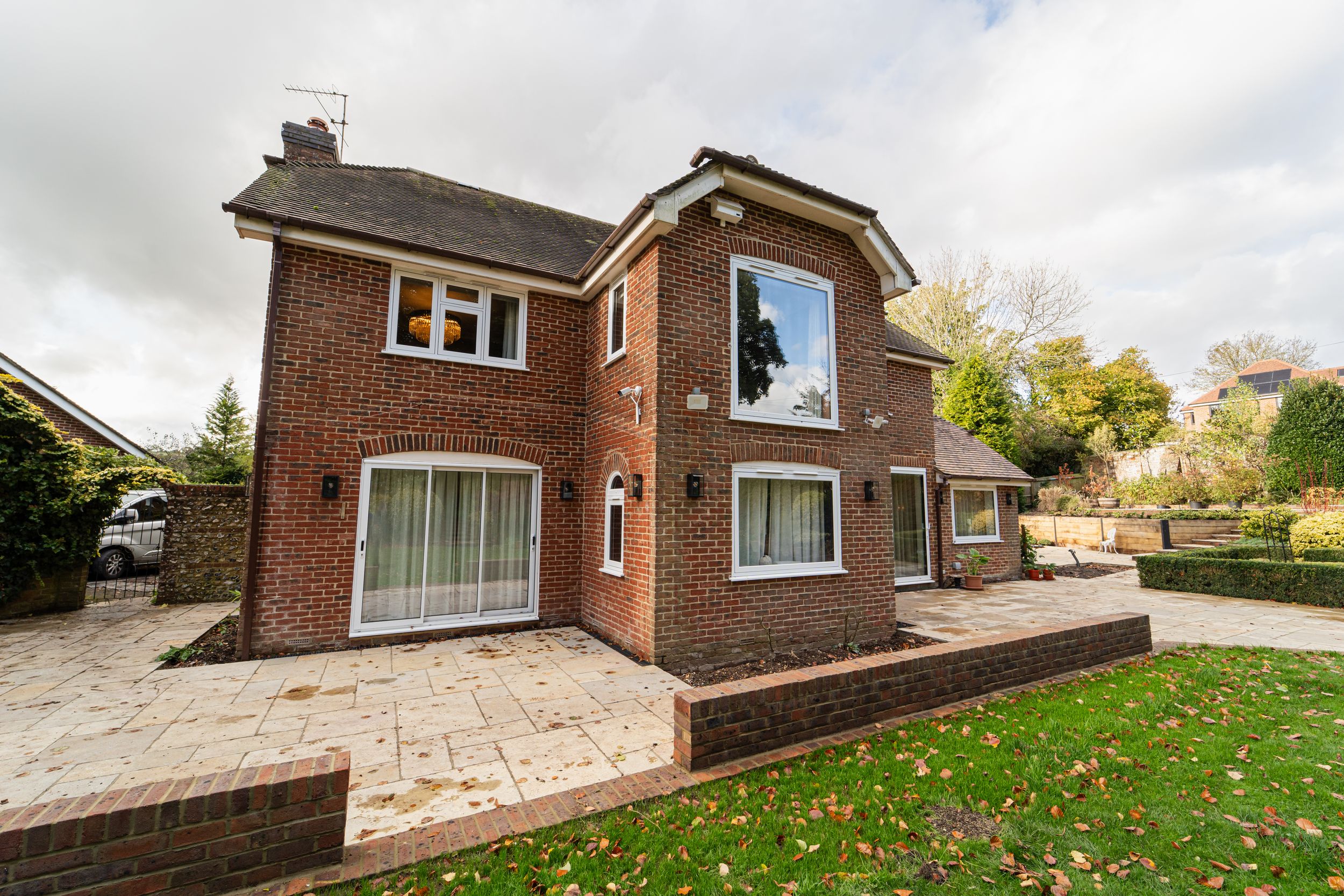 Modern brick house with a curved entrance portico and stone patio overlooking a green lawn on an overcast day.