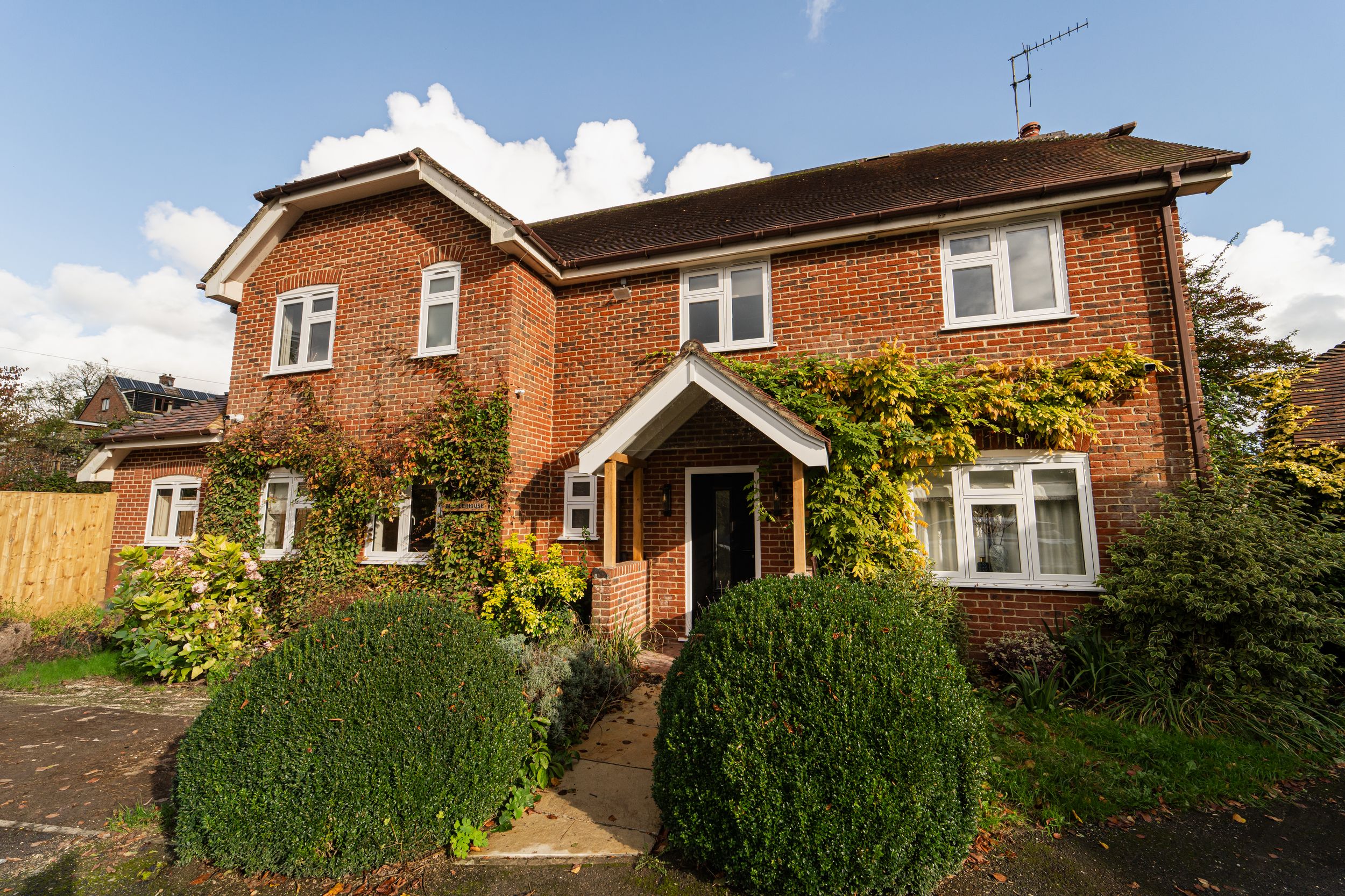 Traditional red brick detached house with green topiary bushes and yellow climbing plants around front entrance porch.