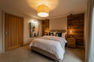 Cozy modern bedroom with wood accent wall, drum pendant light, and plush white bedding in warm neutral tones.
