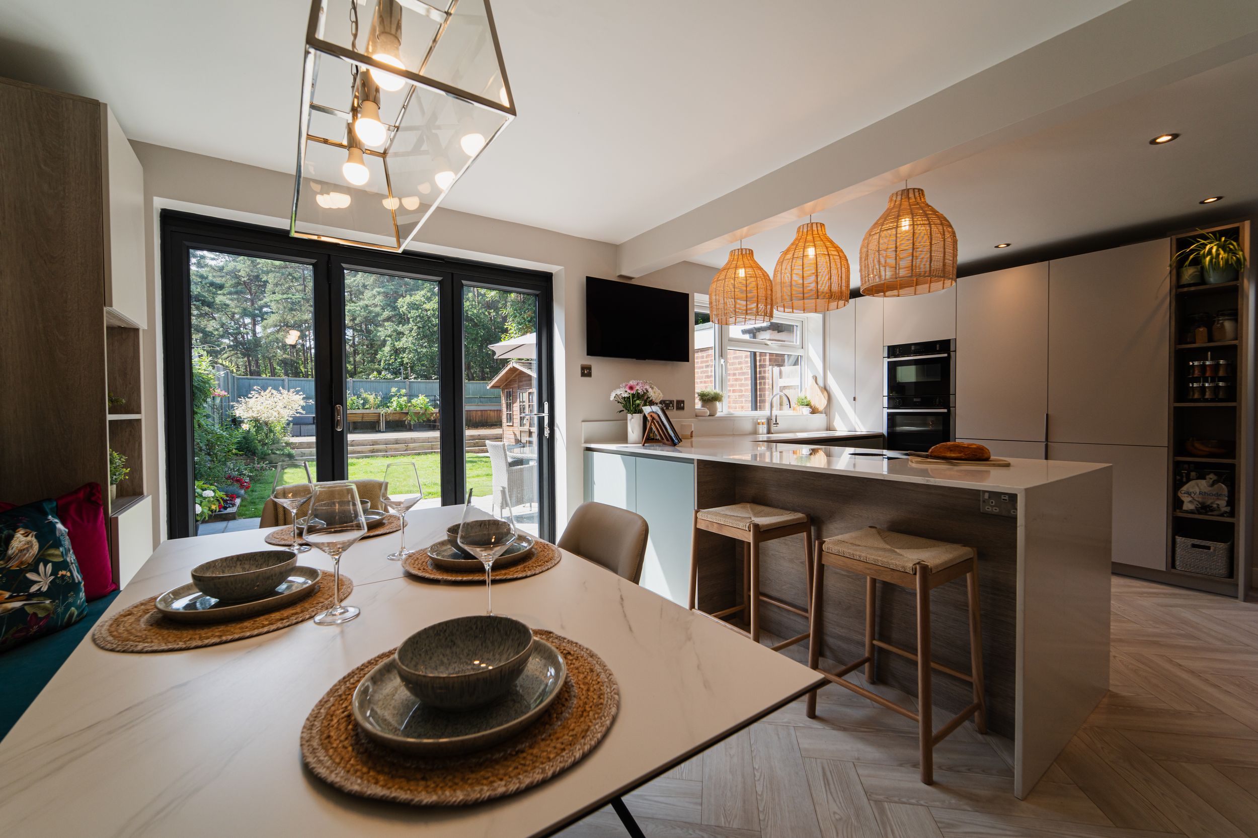 Modern open concept kitchen and dining area with glass windows, pendant lights, and contemporary furniture in neutral tones.