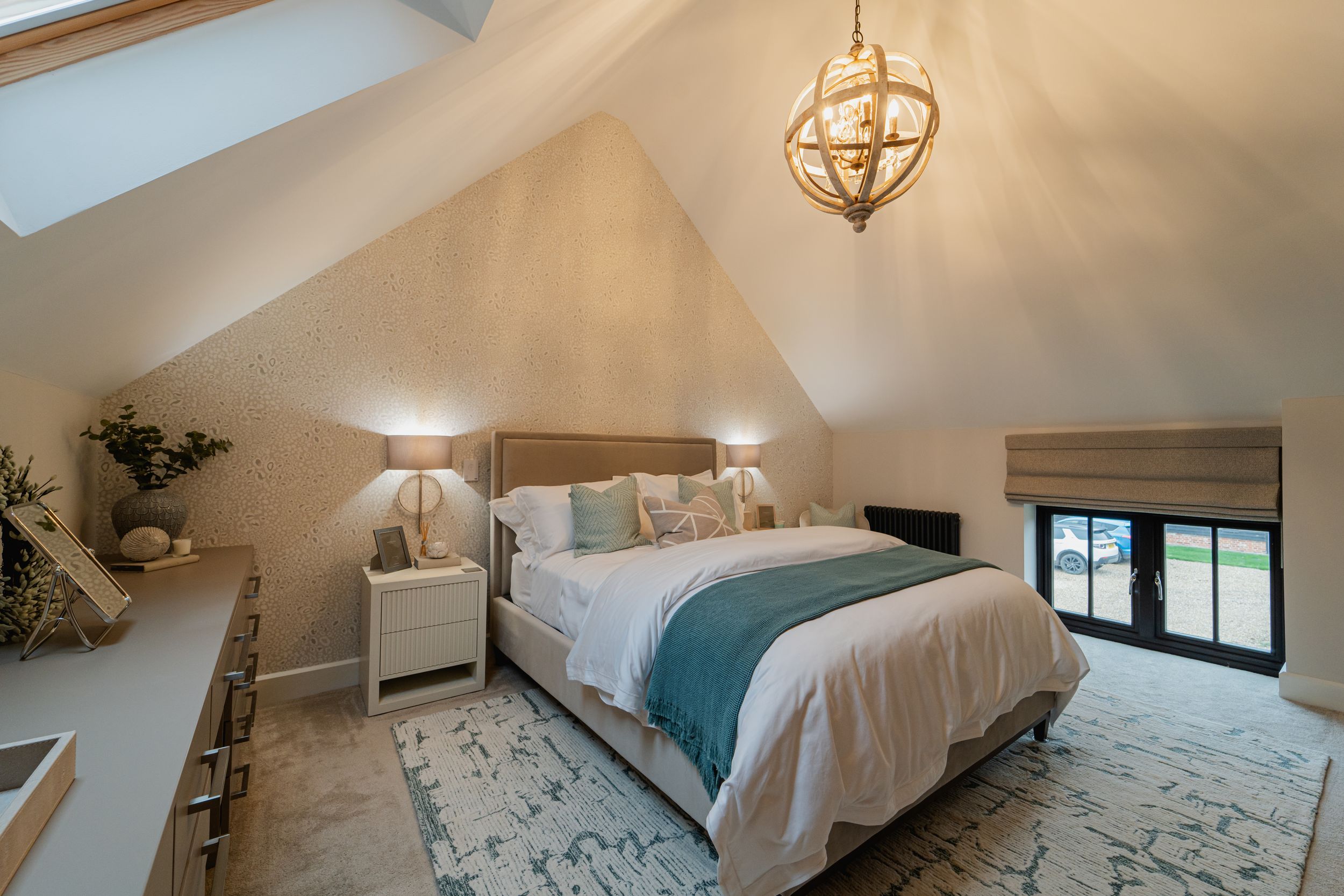 Cozy modern bedroom with vaulted ceiling, spherical pendant light, white bedding and teal accents on plush area rug.