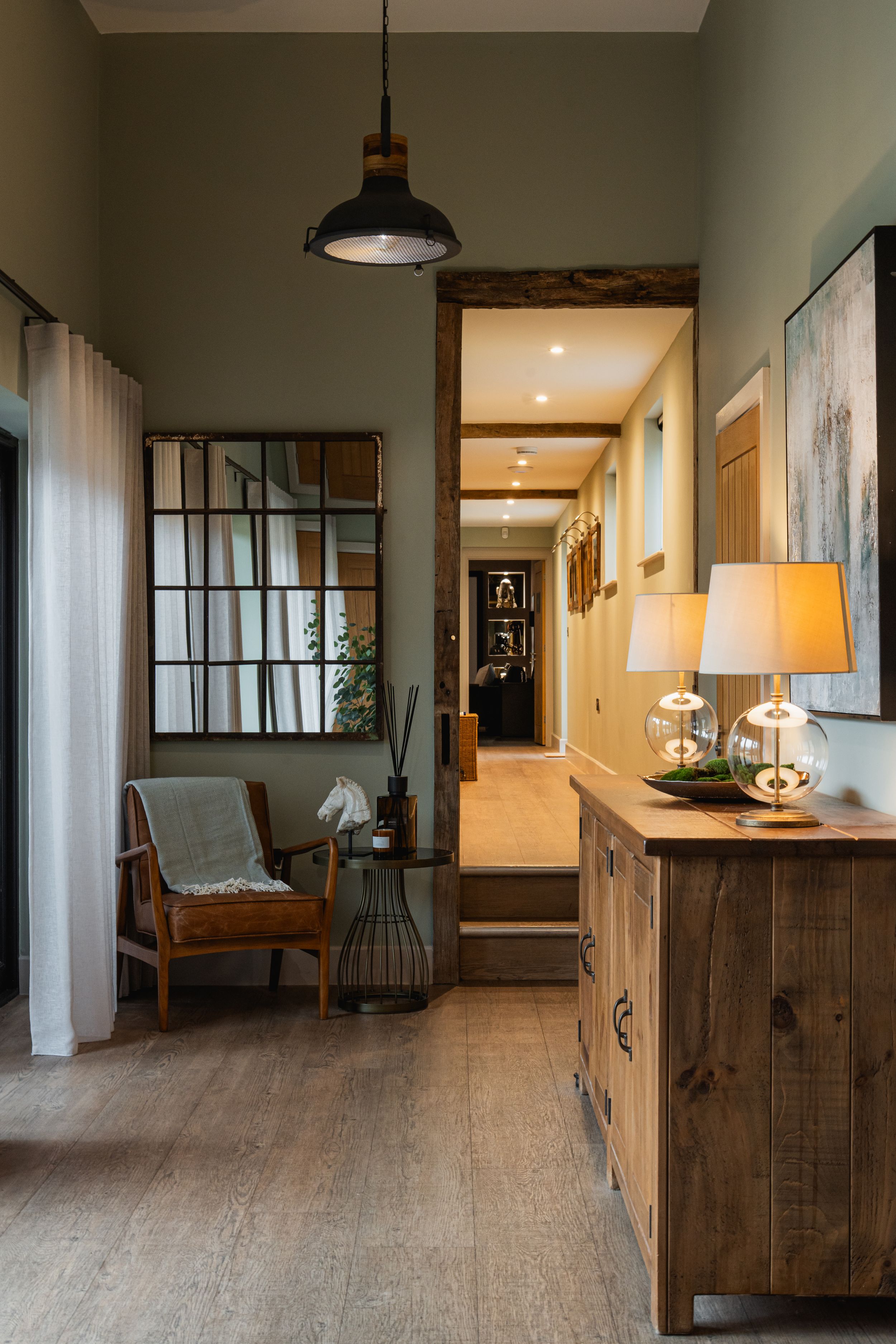 Cozy hallway interior with rustic wood furniture, industrial pendant light, and large mirror creating warm ambiance.