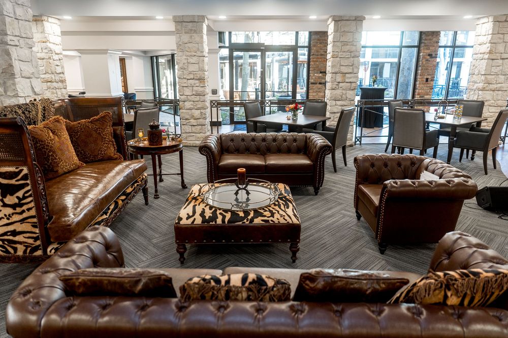 Modern lounge area features brown leather sofas and stone accent walls in an upscale office or business setting.