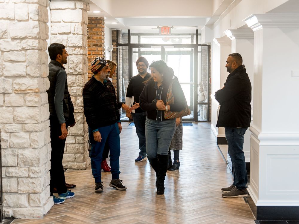People gather and socialize in a modern building hallway with stone columns and natural lighting.