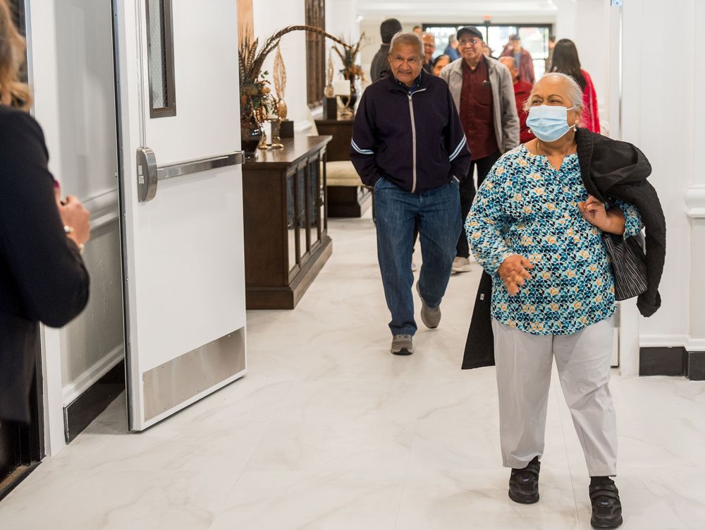 People walking through a bright hallway with white walls and framed artwork displayed.