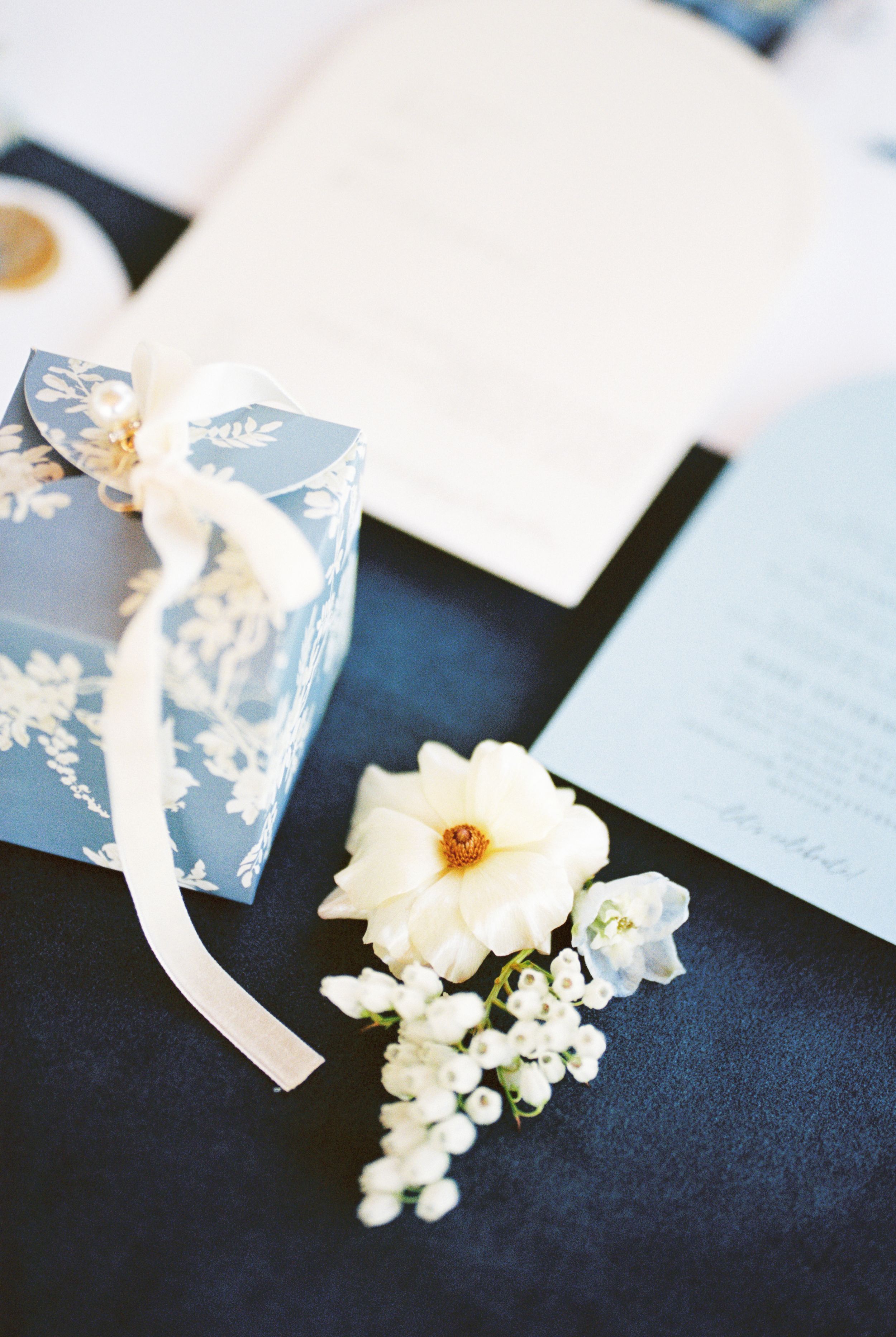 Delicate white floral arrangements and matching paper elements laid out on a dark navy surface for an elegant event.
