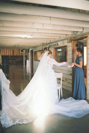 A wedding dress with flowing train being fitted in a rustic indoor space.