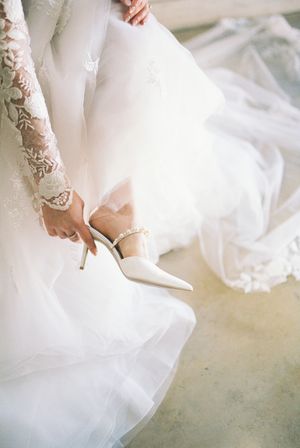 Close-up of bridal shoes being fastened under layers of white tulle and lace.