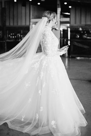 A bride in a lace wedding dress with flowing veil spins in an elegant ballroom setting.
