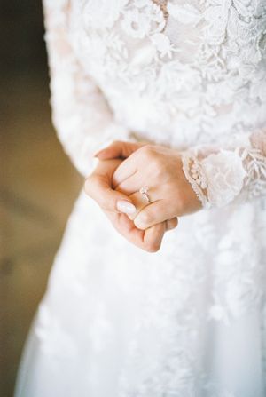 Close-up of delicate lace sleeves and an engagement ring on clasped hands.