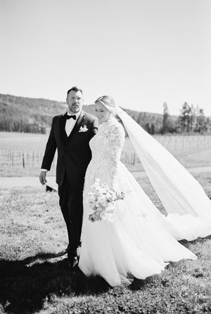 A couple poses outdoors in wedding attire against a scenic mountain backdrop.