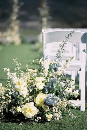 Delicate white and blue floral arrangement decorating an outdoor wedding ceremony chair.