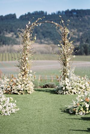 A floral wedding arch with white flowers and greenery stands against a mountain landscape.