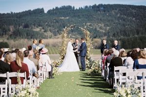 Scenic outdoor wedding ceremony setup with mountain views and white chairs on grassy hillside.