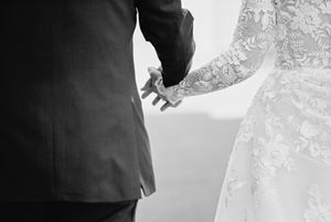 Black and white image of a couple holding hands, showing wedding dress and suit details.
