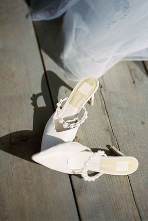 Elegant white bridal heels sitting on a wooden floor beneath layers of tulle.