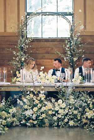 Elegant reception table decorated with lush white and cream floral arrangements and tall candlesticks.
