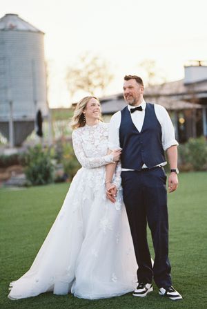 A wedding couple poses near rustic farm silos at sunset.