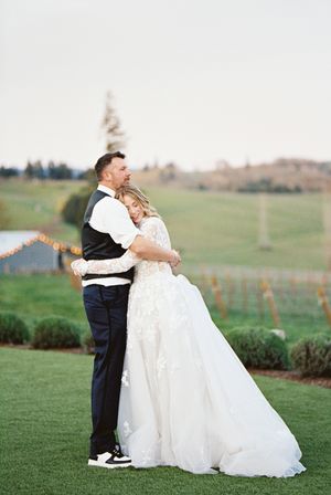 Wedding couple embracing on a rolling green hillside during sunset.