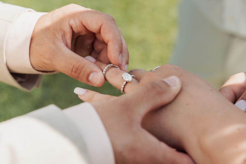 Close-up shot of hands exchanging wedding rings during an outdoor ceremony.