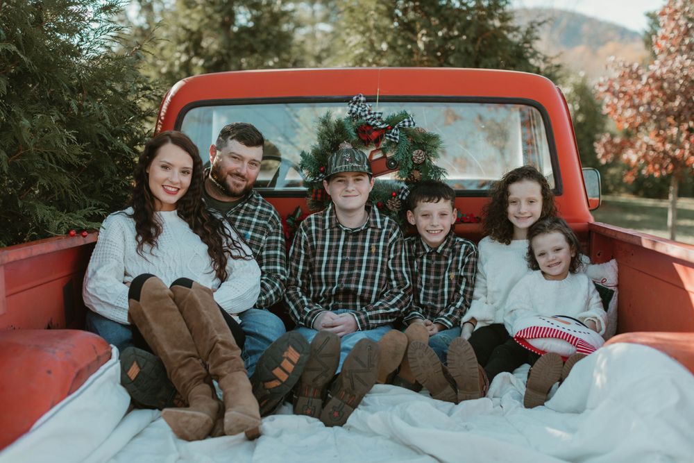 Family sitting together in the bed of a vintage red pickup truck during an autumn photoshoot.