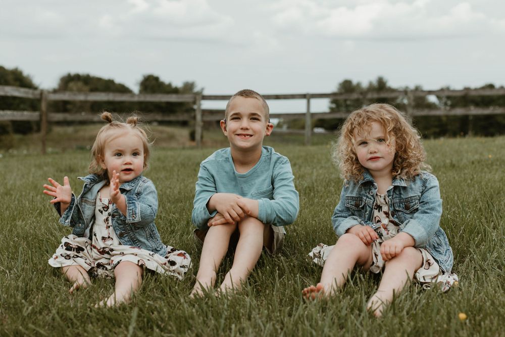 Children sitting together on grass during an outdoor family photo session.