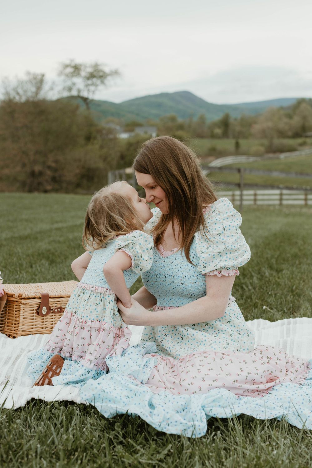 Two people in floral dresses sitting on picnic blanket in spring meadow.