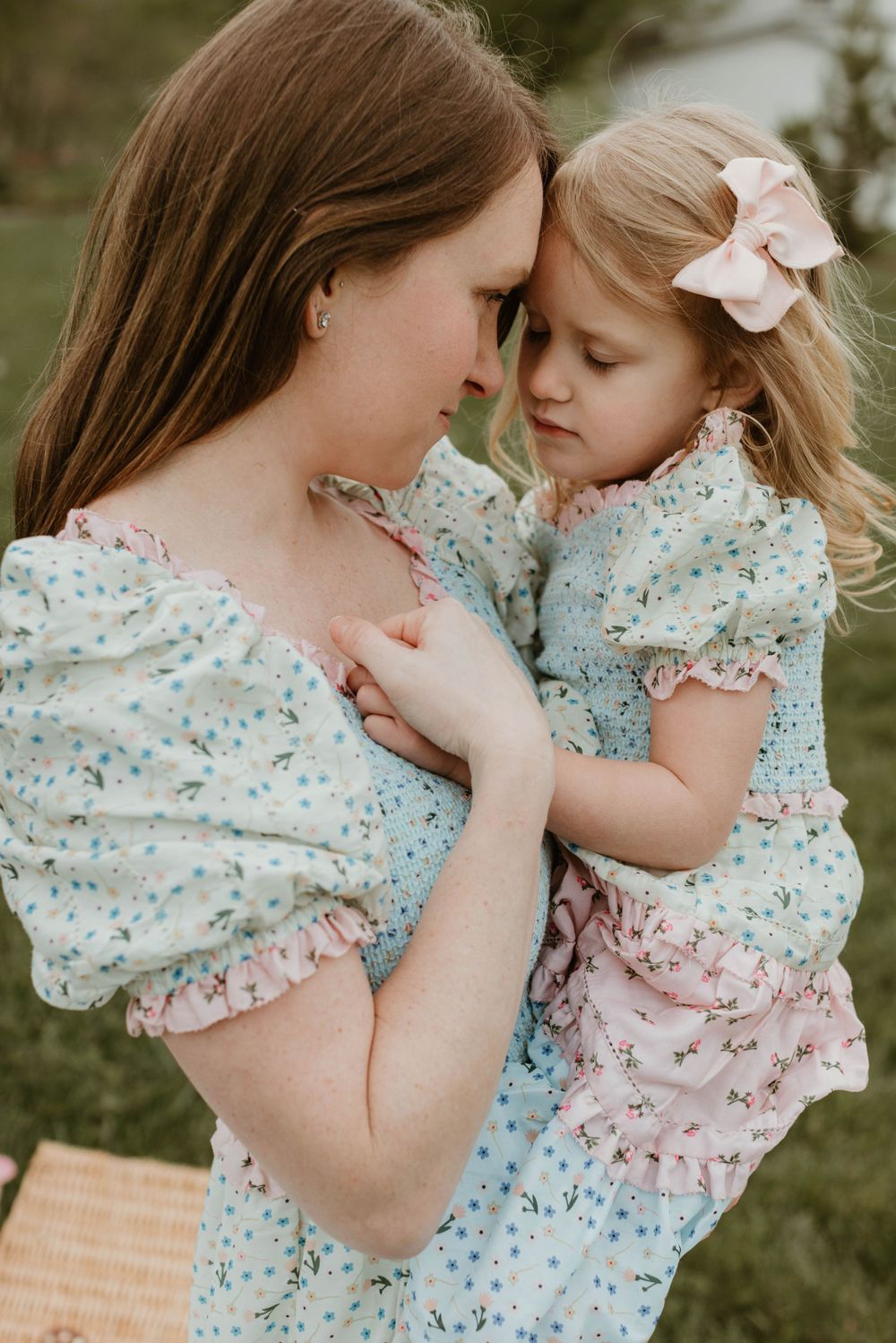 Sweet candid moments captured on a grassy hillside with matching floral spring dresses.