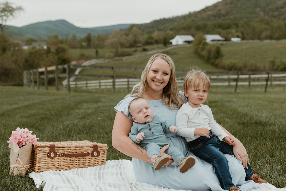 Family photo session in a pastoral setting with picnic basket and mountain views.